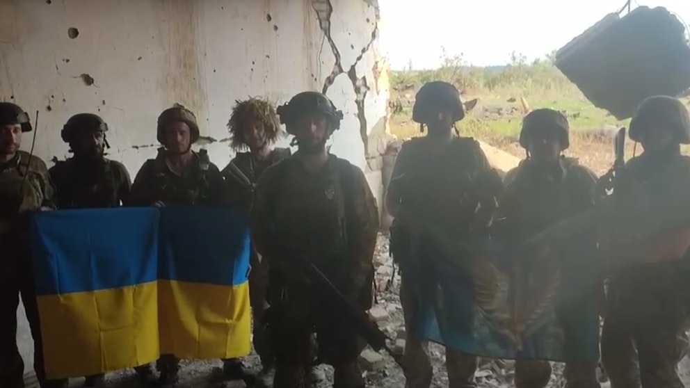 Åtta ukrainska soldater står på rad och håller upp en ukrainsk flagga. 