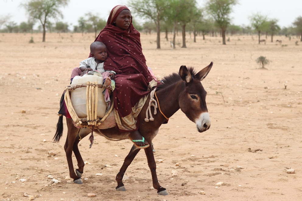 Kvinna på flykt sittandes på en åsna tillsammans med sitt barn.