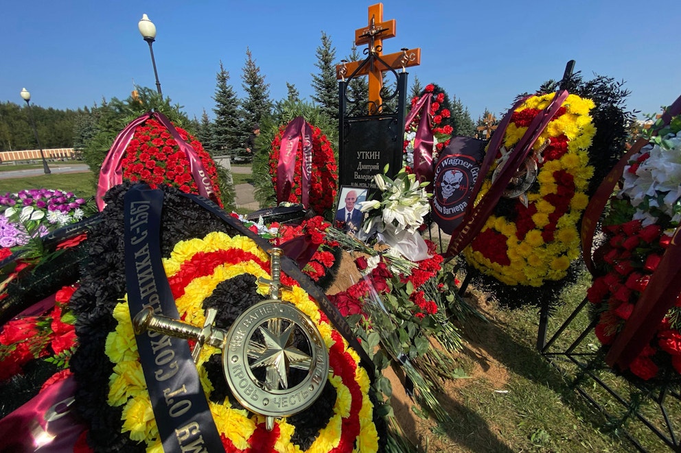 Bild på Utkin, stora blomsterarrangemang och en Wagnerflagga intill gravstenen