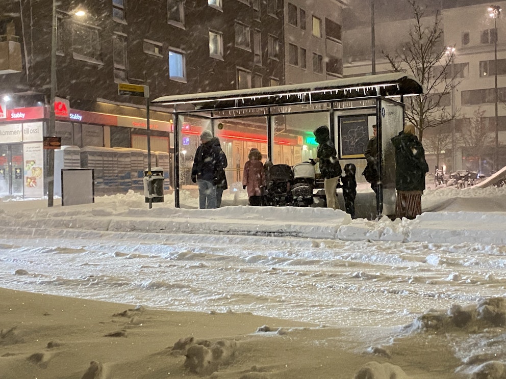 Resenärer på en busshållplats i snöovädret.