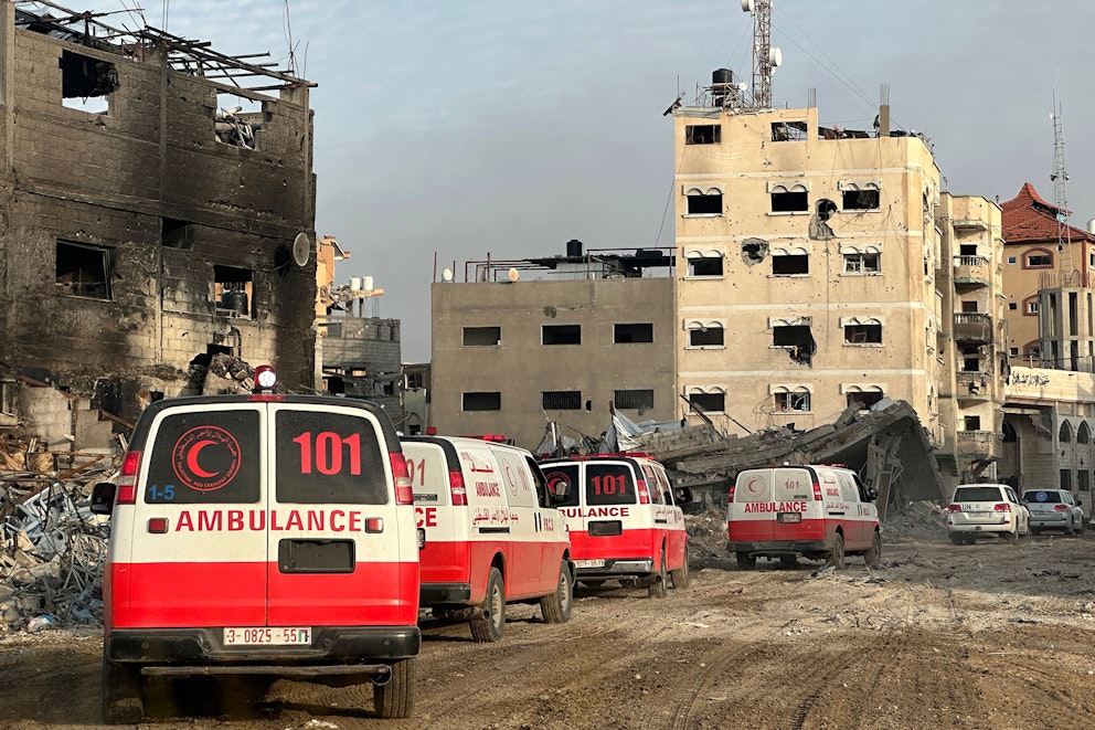 Fyra röda och vita ambulanser kör på led genom ett krigshärjat Gaza.
