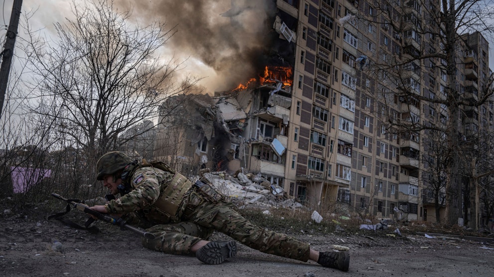 En ukrainsk polis gömmer sig framför en brinnande byggnad.