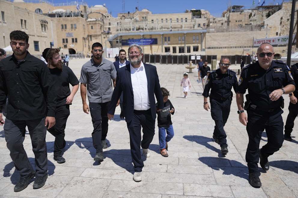 En leende Ben-Gvir i kostym promenerar, tillsammans med säkerhetspersonal och andra israeler