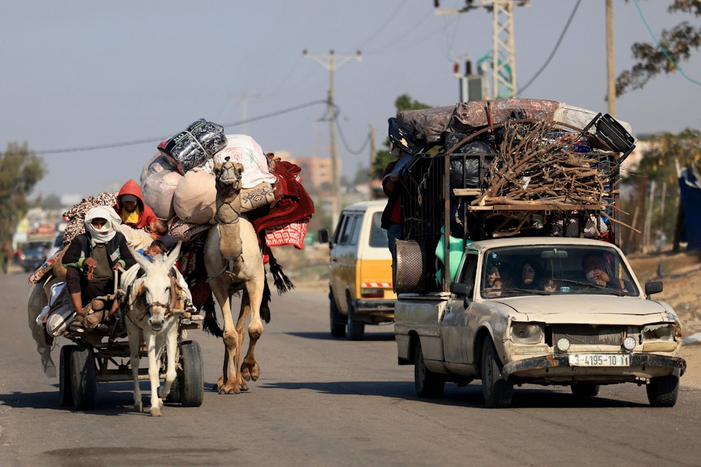 Till vänster en åsna med ett tungt packat ekipage och en kamel med packning på ryggen. Till höger en vit pick-up som har ett fullpackat släp. Flera personer är i ekipaget och i bilen.