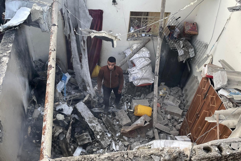 En man står bland bråte i sitt söndertrasade hem med uppgiven blick.