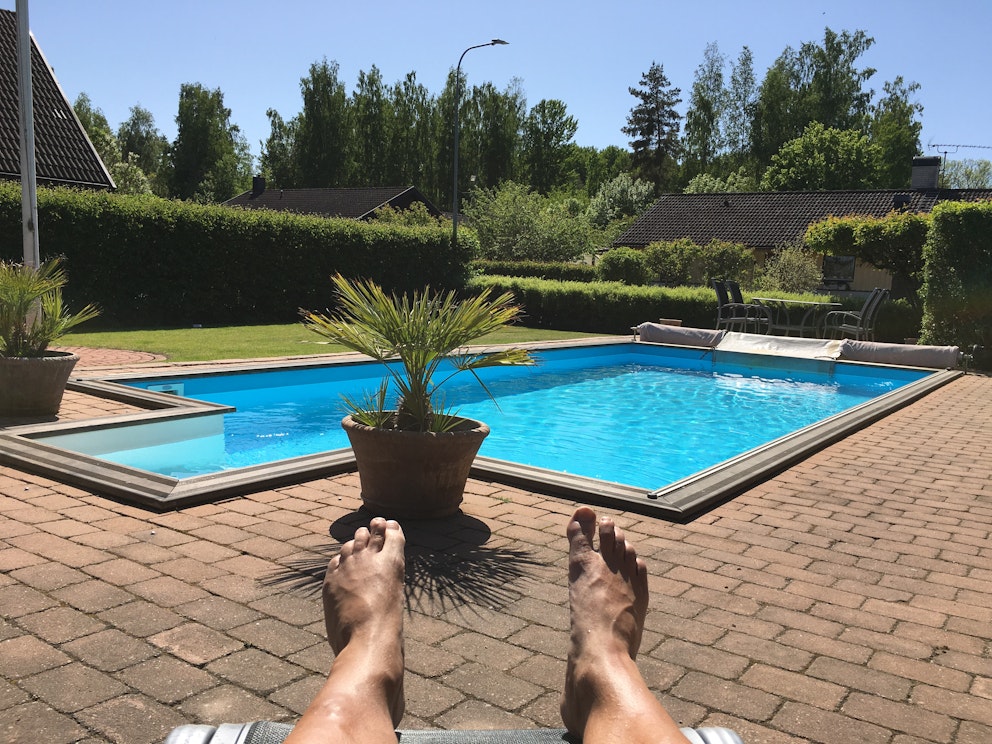 En pool är i fokus och i förgrunden syns ett par fötter som ser ut att tillhöra en person som solar.