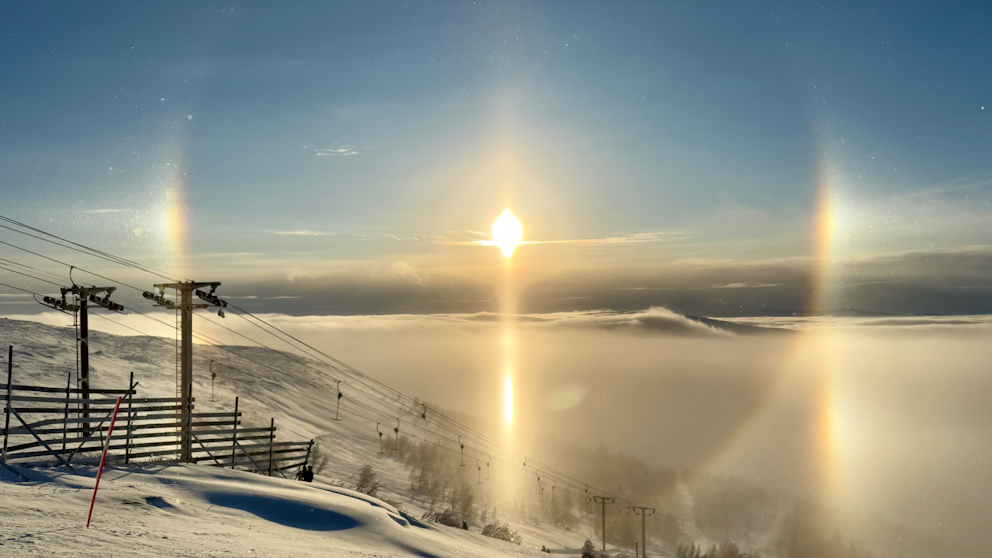 Solig vinterdag i skidbacken med en tydlig halo-effekt runt solen och liftstolpar i förgrunden, Åre.