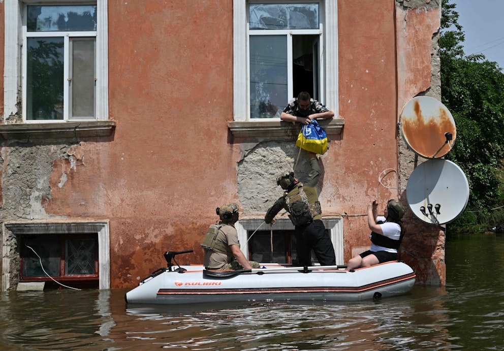 Militärpersonal ur Ukrainas nationalgarde levererar en påse med mat till en person genom ett fönster. Vattnet har stigit så pass högt att militärpersonalen behöver färdas i gummibåt.