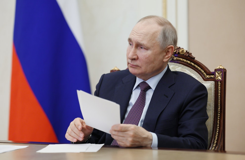 Bilden visar Rysslands president Vladimir Putin som sitter vid sitt skrivbord och håller en bunt papper.