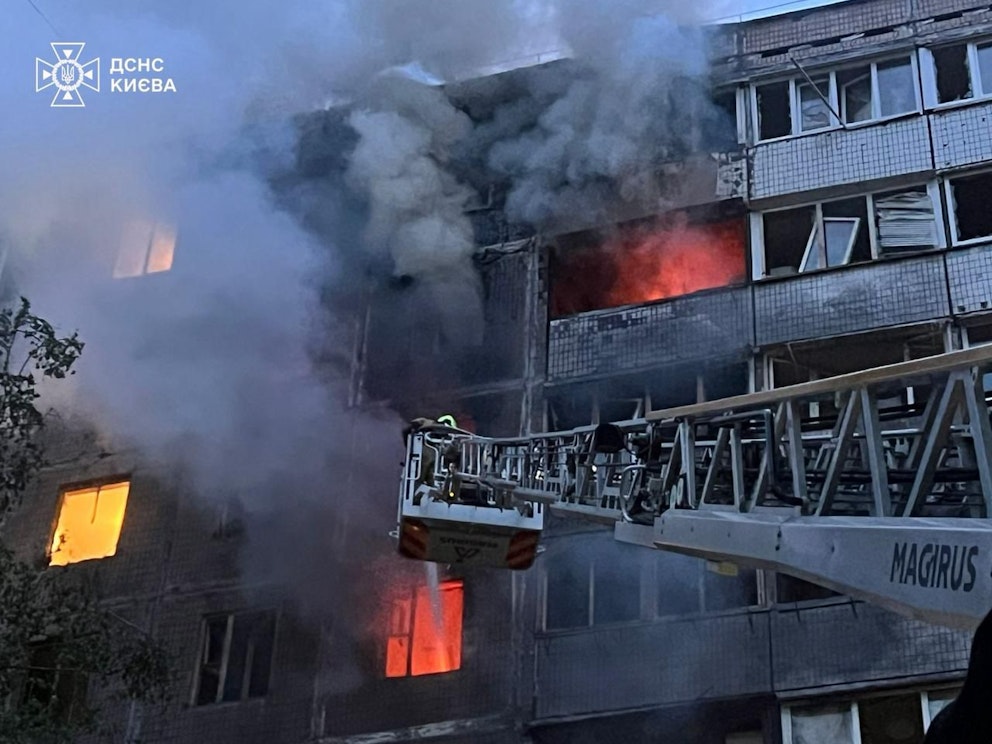 En person från Ukrainas räddningstjänst hissas upp i en korg för att släcka en brand i ett bostadshus efter ryska attacker mot staden.